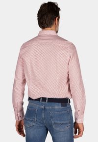 Rood en wit gestreept shirt met lange mouwen en een button-down kraag, gedragen met een blauwe jeans. Heeft een subtiel geometrisch patroon.