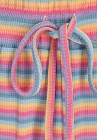 Multikleurige ribstof met pastelkleurige strepen in roze, geel, blauw en paars. Bevat een gestrikte trekkoord bij de elastische taille.