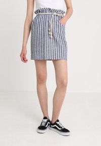 Pruhovaná džínová sukně se shromážděným páskem a šňůrkou na stažení. Má boční kapsy a vypasovaný střih. Nenosí se s černými teniskami.