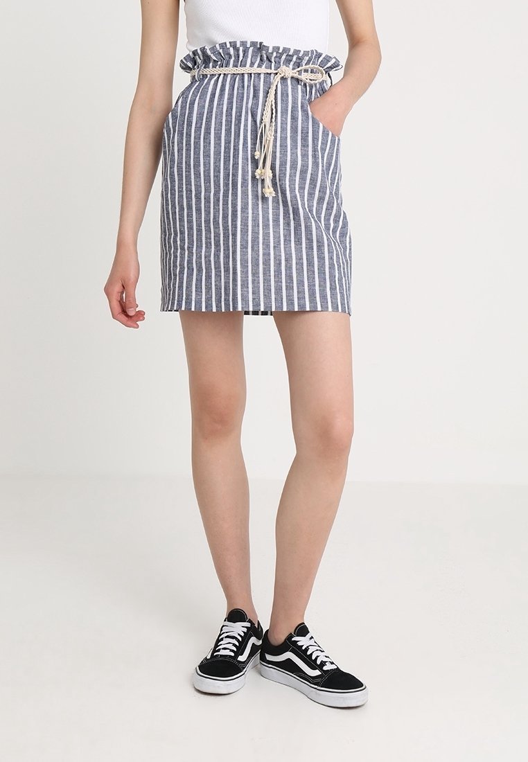 Pruhovaná džínová sukně se shromážděným páskem a šňůrkou na stažení. Má boční kapsy a vypasovaný střih. Nenosí se s černými teniskami.
