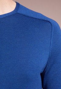 Blue knitted sweater featuring a round neckline, textured ribbing, and a reinforced shoulder seam for durability.