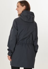 Mörkgrå, vattentät jacka med huva, elastiskt dragsnöre i midjan och en logotyp på vänster axel. Slät, matt yta.