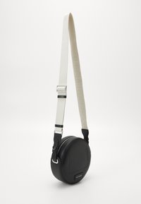 Svart runt axelväska med silverdragkedja och justerbar bred vit rem med präglat varumärke.