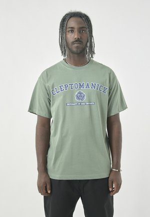 Green cotton T-shirt with a loose fit, featuring "CLEPTOMANICK" in bold blue lettering and a graphic of a lion. Short sleeves and crew neck.
