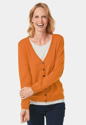 Gilet orange avec un col en V, des manches longues et des boutons bleus, porté sur une chemise blanche ; fabriqué dans un tissu doux avec une texture lisse.