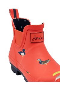 Botte de cheville en caoutchouc rouge avec des illustrations de canards, semelle noire et logo de marque. Tige texturée avec une languette pour un enfilage facile.
