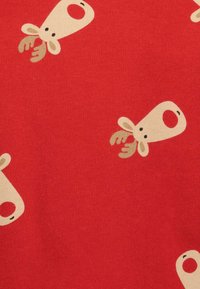 Un tessuto rosso con un motivo ripetuto di teste di renna beige con corna e nasi rotondi, che mostra una superficie liscia.
