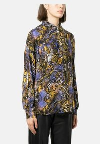 Blusa a maniche lunghe con un vivace motivo a stampa serpente nei toni del viola, oro e nero, dotata di chiusura con bottoni davanti e colletto.