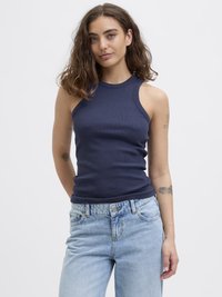 Marineblå ribbet ermeless topp med høy hals, parret med lyseblå, litt løse denimjeans med knappelukking og frontlommer.