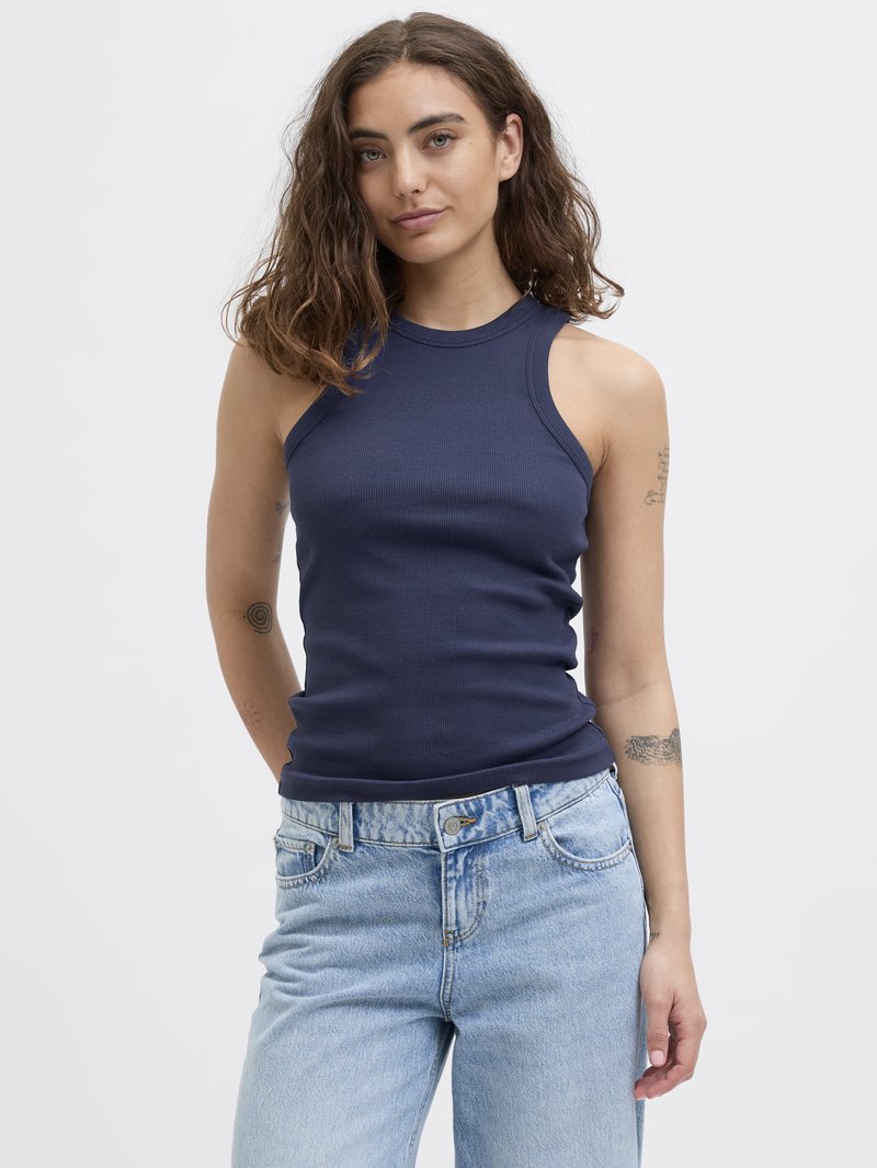 Marineblå ribbet ermeless topp med høy hals, parret med lyseblå, litt løse denimjeans med knappelukking og frontlommer.