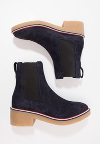 Botines de ante azul marino con paneles laterales elásticos negros, puntera redondeada y un tacón de bloque de goma color beige con ribete rojo y blanco.