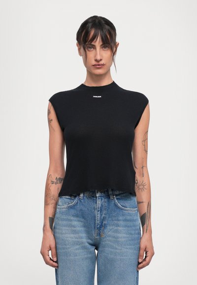 Sort, ærmeløs crop top lavet af ribbet stof med høj hals. Har et lille mærke logo på forsiden. Bæres med blå jeans.