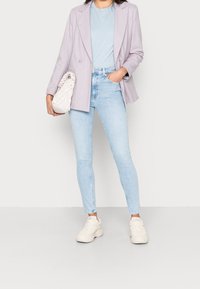 Blazer doble faz en un tono púrpura claro sobre una camiseta azul clara, combinado con jeans ajustados azul claro y zapatillas blancas; sosteniendo un bolso beige.