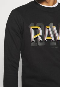 Felpa nera con una grande e audace grafica "RAV" in lettere tridimensionali multicolori, con colletto e polsini a coste.