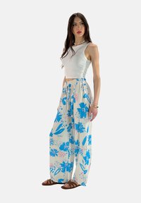 Vit ärmlös crop top i kombination med vida byxor med blommönster i blått och rosa, med elastisk midja och lätt material.
