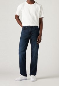 White cotton t-shirt paired with dark blue jeans. The jeans have a straight cut, classic five-pocket design, and are worn with white sneakers.