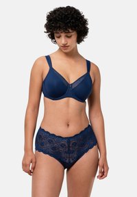 Tummansininen rintaliivi, jossa on sileä kangas, läpikuultavia yksityiskohtia ja tukevat langat. Hieman tummansiniset pitsialushousut, joissa on aallotetut reunat ja monimutkaiset kuviot.