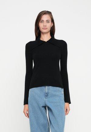 Svart langermet topp med en overdimensjonert krage, tettsittende kropp og ribbet tekstur, kombinert med lyseblå denim jeans.