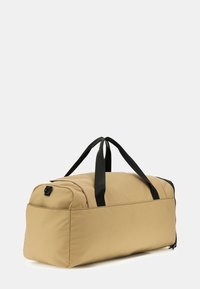 Beige Duffel Bag aus strapazierfähigem Stoff mit schwarzen Akzenten, doppelten Griffen, einem Reißverschluss und rechteckiger Form.