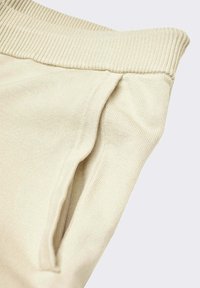 Tejido de punto beige con una cinturilla acanalada y un bolsillo lateral. La textura es suave y con un ligero estiramiento para mayor comodidad.