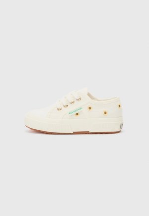 Canvas sneakers i krämfärg med guldtonade öglor, grön logotyp och brun gummisula. Har prickiga detaljer på sidorna. Lågt snitt.