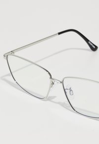 Lunettes en métal argenté avec des verres transparents. Design angulaire, branches fines avec des accents texturés noirs et plaquettes de nez ajustables.