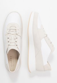 Scarpe sportive bianche e beige realizzate in pelle e camoscio con una suola in gomma spessa, dotate di lacci e design minimalista.