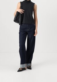 Top nero a colletto alto, jeans a gamba larga blu scuro con orli risvoltati e décolleté neri a punta. È presente una borsa a tracolla in pelle nera.