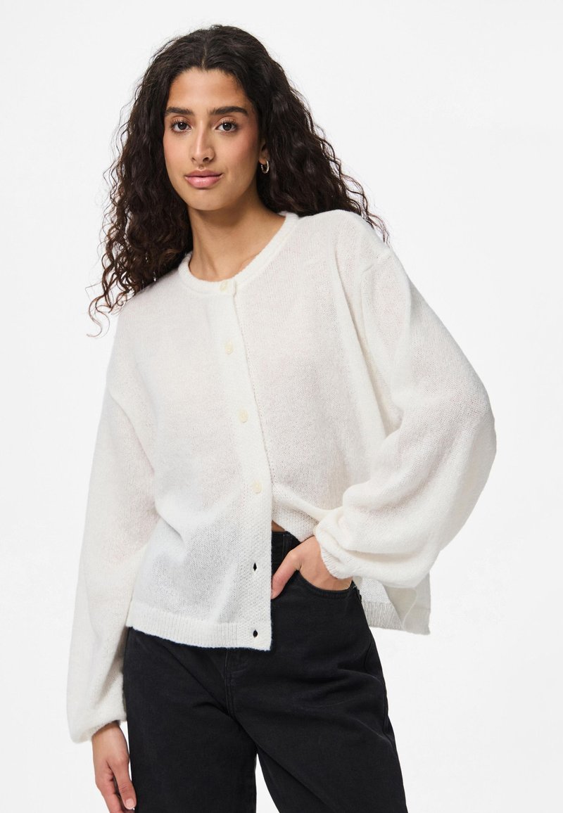 Cardigan blanc en maille avec une coupe décontractée, présentant un col rond, des fermetures à boutons et des manches longues volumineuses.