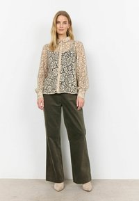 Lace blouse with a collared neckline, featuring intricate floral patterns in cream and black, paired with olive green wide-leg pants and beige shoes.