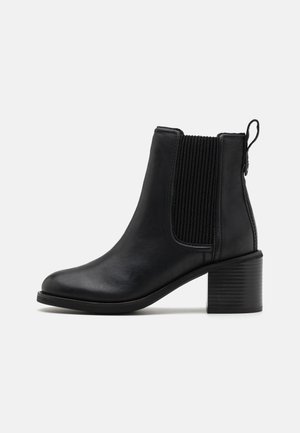 Musta nahkainen nilkkaboots, jossa on uurrettuja joustavia sivupaneeleja, minimalistinen muotoilu, pyöristetty kärki ja teksturoitu lohkokorko.