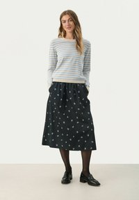 Stribet blå og beige sweater med rund halsudskæring, parret med en sort nederdel med blomstermønster og lommer. Sorte loafers bæres.