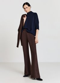 Marineblauer gerippter Rollkragenpullover, lässiger Schnitt; kombiniert mit braunen Schlaghosen aus glattem Stoff; elegante schwarze spitze Schuhe.