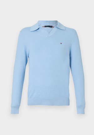 Pull en tricot bleu clair à manches longues avec un col en V et un petit logo Tommy Hilfiger sur la poitrine gauche.