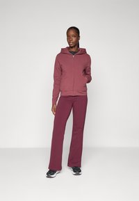 Karmīnsarkans zip-up kapucis ar kapuci un priekšējām kabatām, apvienots ar saskaņotām karmīnsarkanām platām biksēm. Materiāls izskatās mīksts un ērti pieguļošs.