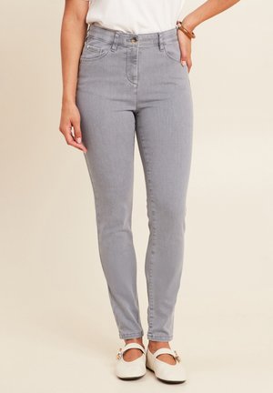 Jean gris taille haute au coupe ajustée, avec deux poches avant et une fermeture à bouton, associés à des ballerines blanches.