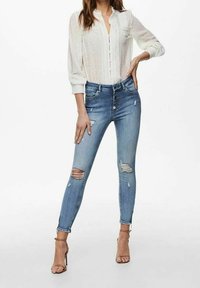 Slim fit jeans i ljusblå denim med slitna detaljer, med hög midja och flera knäppningar fram. Kombineras med en vit blus.