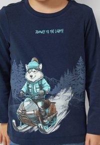 Marineblaues Langarm-T-Shirt mit einem Cartoon-Husky auf einem Schneemobil, mit einem hellblauen Design, einer strukturierten Berglandschaft im Hintergrund und dem Text „Reise zu den Lichtern!“