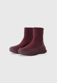 Bottines bordeaux avec un dessus lisse et extensible, et une semelle épaisse et texturée, arborant un branding discret sur le côté extérieur.