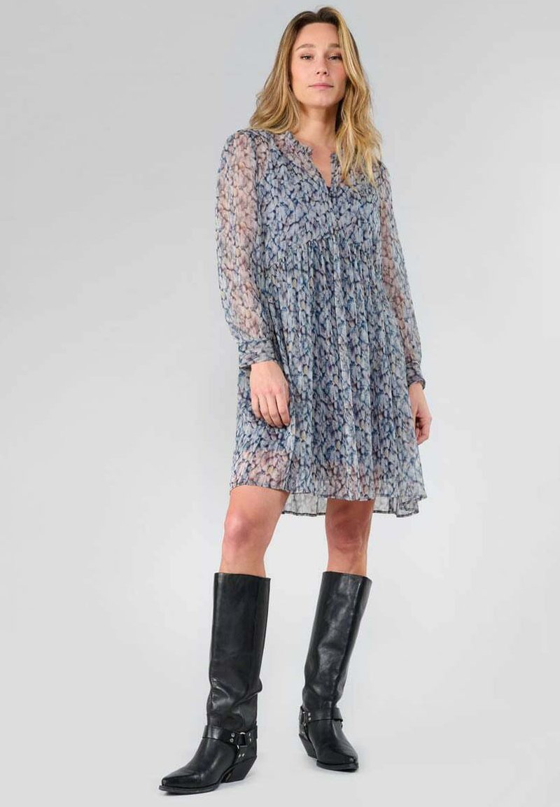 Vestido ligero con estampado en tonos azules, mangas largas y translúcidas, y cintura fruncida, combinado con botas de cuero negro hasta la rodilla.