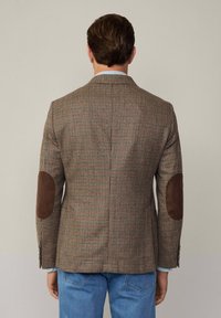 Blazer im Schäfchenmuster in Braun und Creme mit braunen Lederbesätzen an den Ellbogen, taillierte Passform und seitlichem Schlitz am Rücken.