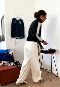 Personne en tenue Adidas noire et blanche arrange des vêtements pliés sur une petite table à côté d’un mur blanc avec un maillot de sport suspendu.
