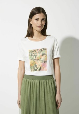 White T-shirt with short rolled sleeves, featuring a colorful floral print design and the text "my garden plenty of joy" in the center. Paired with a green, pleated skirt.
