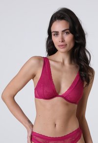 Reggiseno con pizzo a contrasto, scollatura a V profonda in fucsia acceso, realizzato in tessuto morbido e con supporto con ferretto, caratterizzato da spalline larghe e un motivo decorativo.
