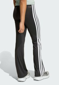 Crne atletske hlače s bijelim vertikalnim prugama, izrađene od glatkog, fleksibilnog materijala s prilagođenim krojem i suptilnim logotipom na pojasu.