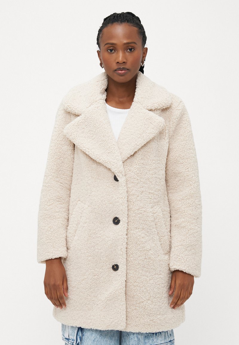Kreemivärvi faux shearling mantel suure krae, eesnööbid ja küljetaskud; vabalt istuv lõige, langenud õlgade ja pehme tekstuuriga.