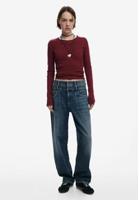 Burgunderfarbener, gerippter Langarm-Pullover, hochgeschnittene, hellblaue, baggy Jeans, schwarze Schuhe mit grünen Akzenten, geschichtete schwarze Halsketten.