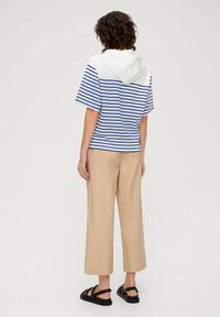 Gestreiftes blauen und weißes kurzärmliges Hoodie, kombiniert mit beigen weitgeschnittenen Hosen und schwarzen Sandalen mit Riemen. Lässiges, entspanntes Design.