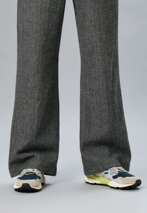 Grå fiskeben bredbenede bukser parret med beige, navy og limegrønne chunky sneakers på en grå baggrund.