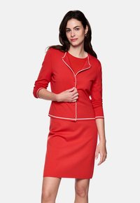 Red cardigan with white trim and buttons, paired with a matching red knee-length skirt. Smooth texture, fitted design, long sleeves.